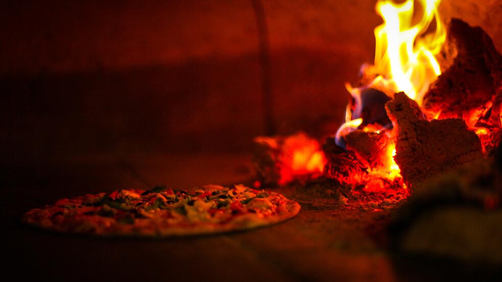 Pizza bakt in een houtgestookte oven met vlammen.
