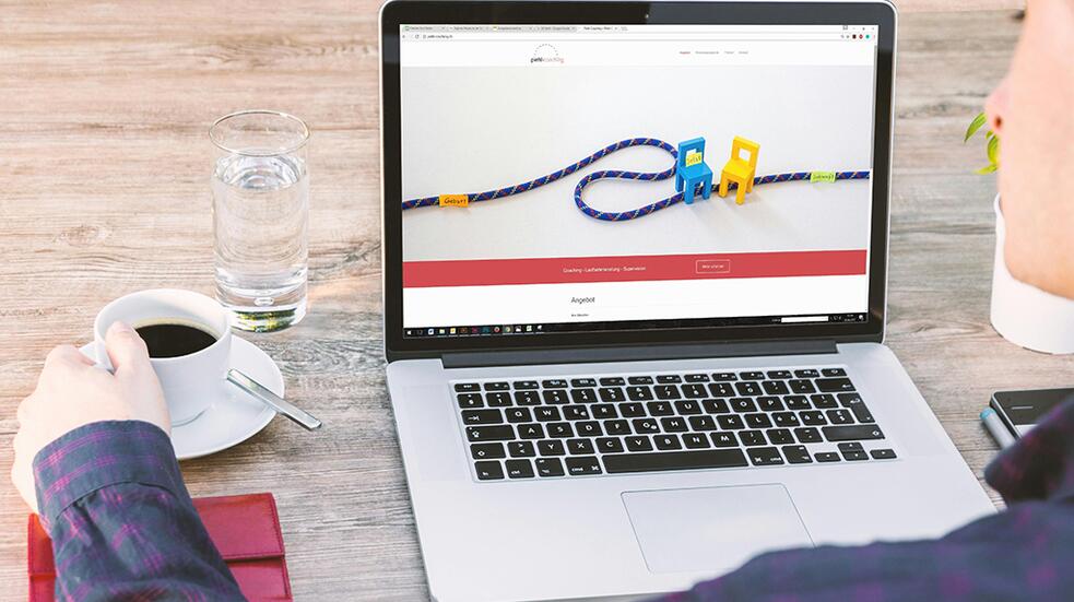 Persoon drinkt koffie bij laptop met kleurig speelgoed op scherm.